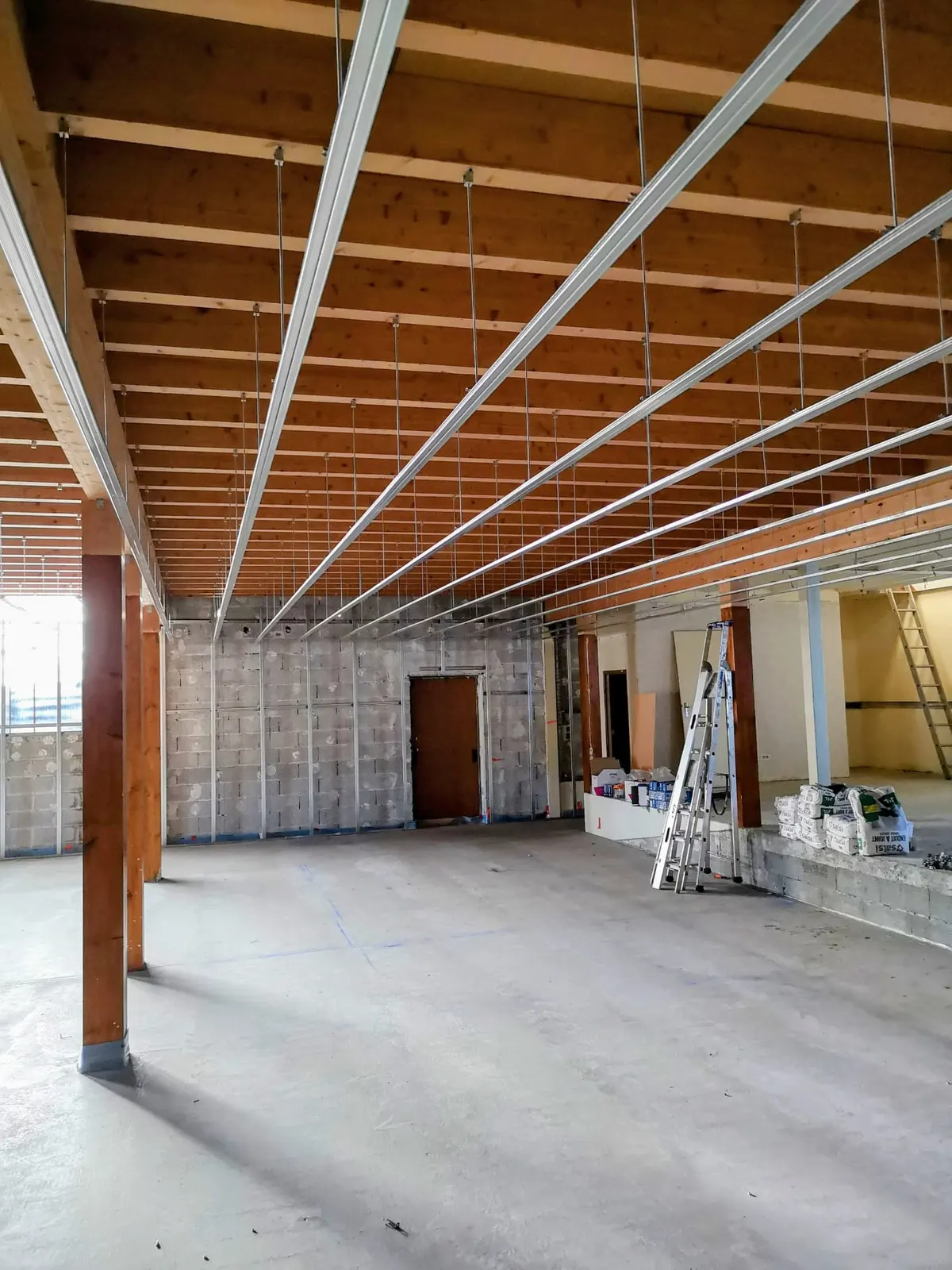 Ossature métallique d'un faux-plafond suspendu posée sur la charpente bois d'un plateau commercial brut, avec gaines de ventilation isolées
